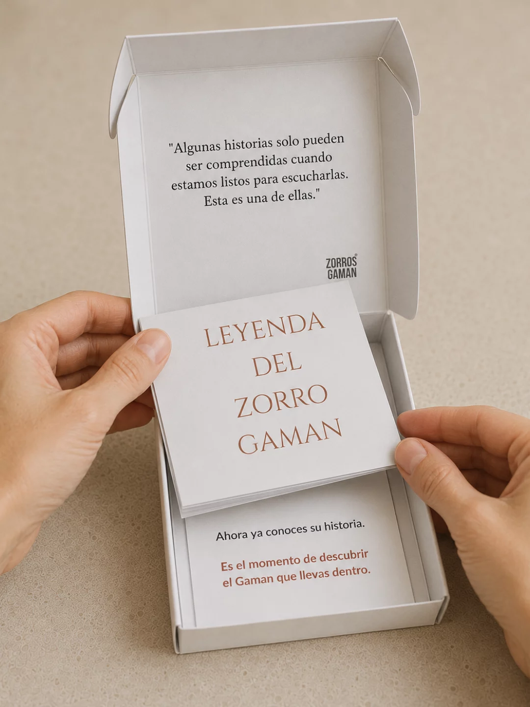 Manos sacando de la caja el librito con la leyenda del Zorro Gaman